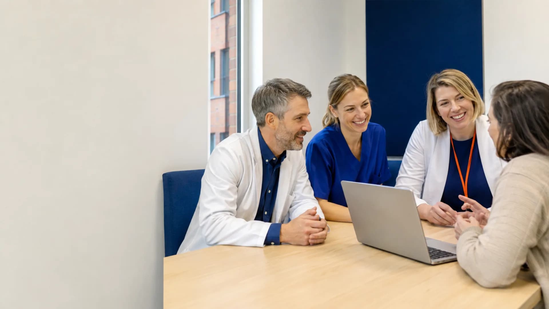 A multidisciplinary care team listening to a patient in a warm modern clinic