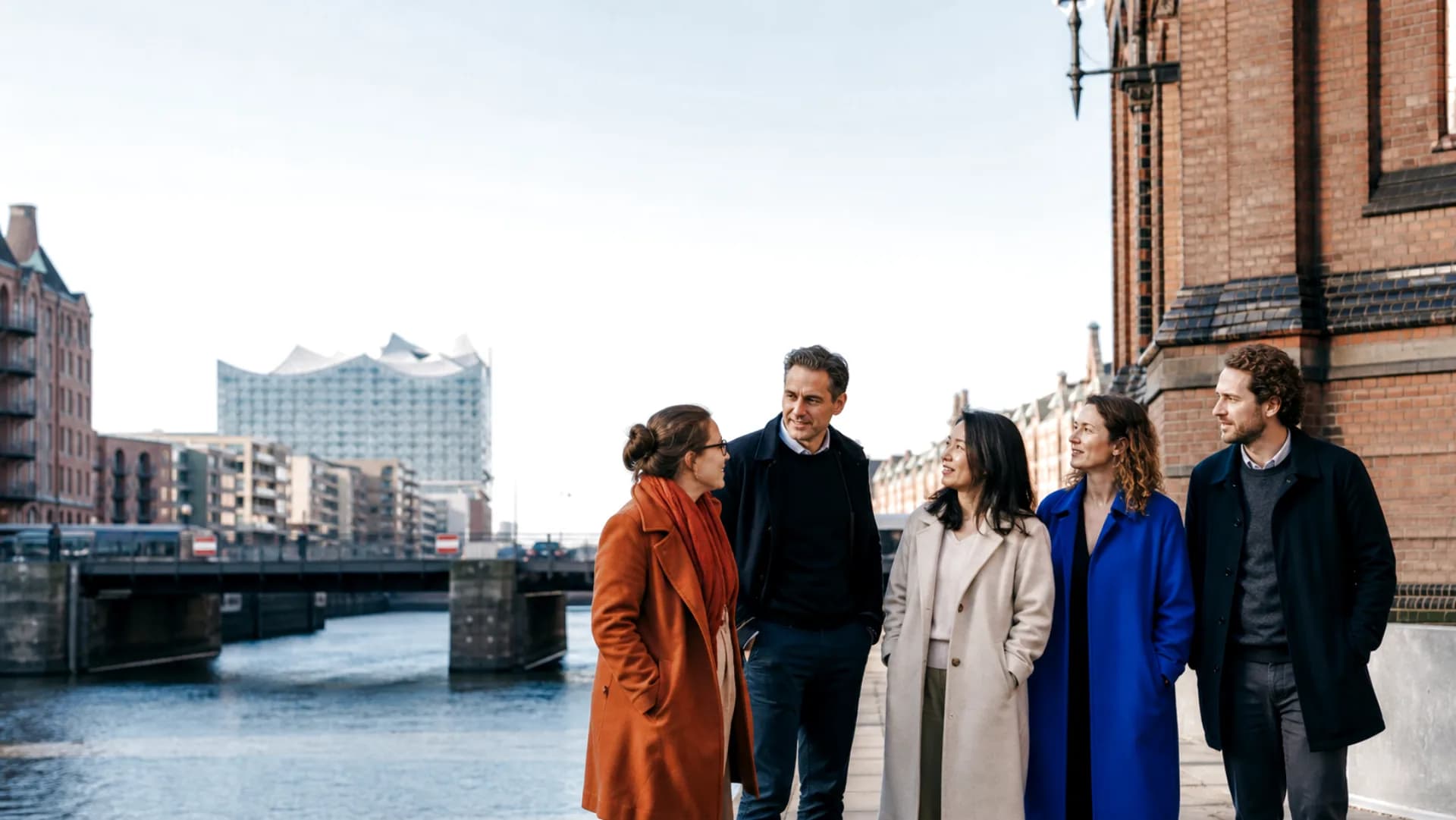 A diverse Dudoxx team walking beside Hamburg’s Speicherstadt with the Elbphilharmonie beyond